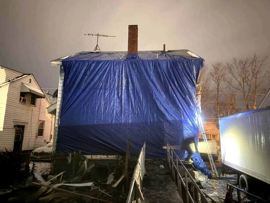 A large blue tarp covering an exposed upper floor after a house fire