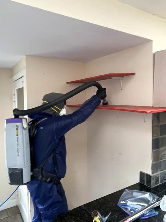 A technician vacuuming wall-mounted shelving with a backpack vacuum