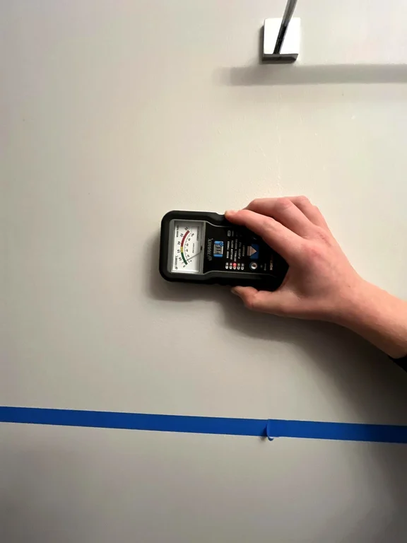 Hand holding a moisture meter against an interior wall