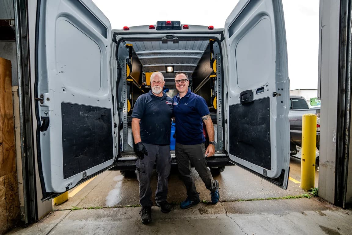 Two Cleveland Water and Fire Restoration, Inc. technicians smiling at the open back of a loaded equipment van
