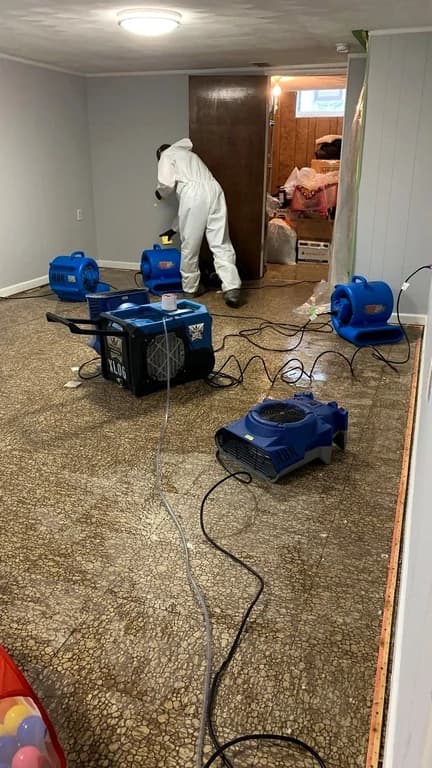 A technician working in a water-damaged room with air movers and drying equipment