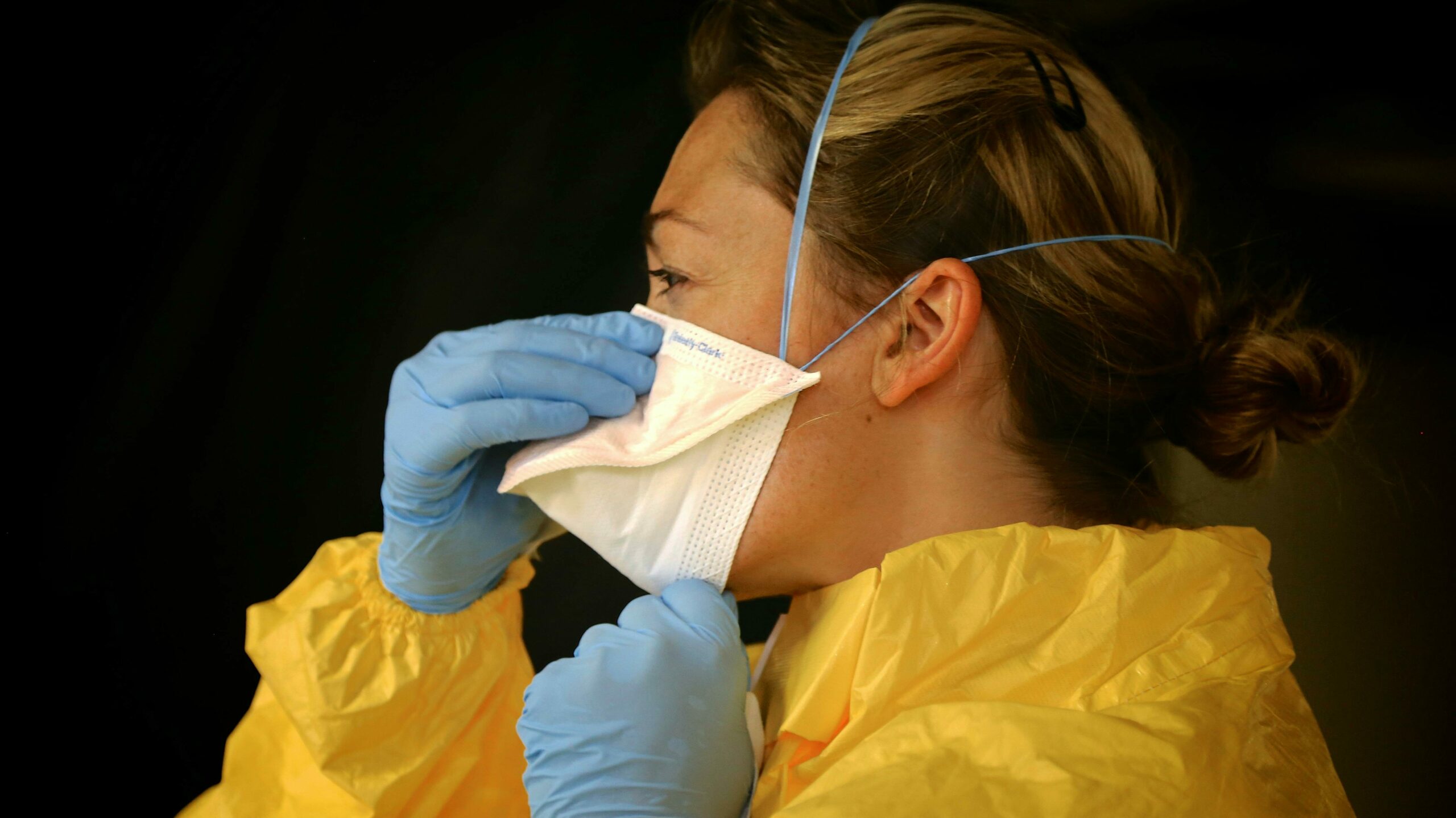 A person wearing PPE- in yellow smock, blue gloves, and a white mask